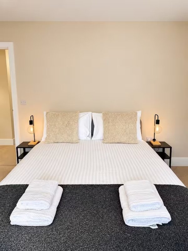 Bedroom with double bed, two bedside lamps, decorative pillows and folded towels