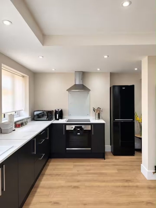 Modern kitchen with black cabinetry, white countertops, stainless steel range hood and black appliances
