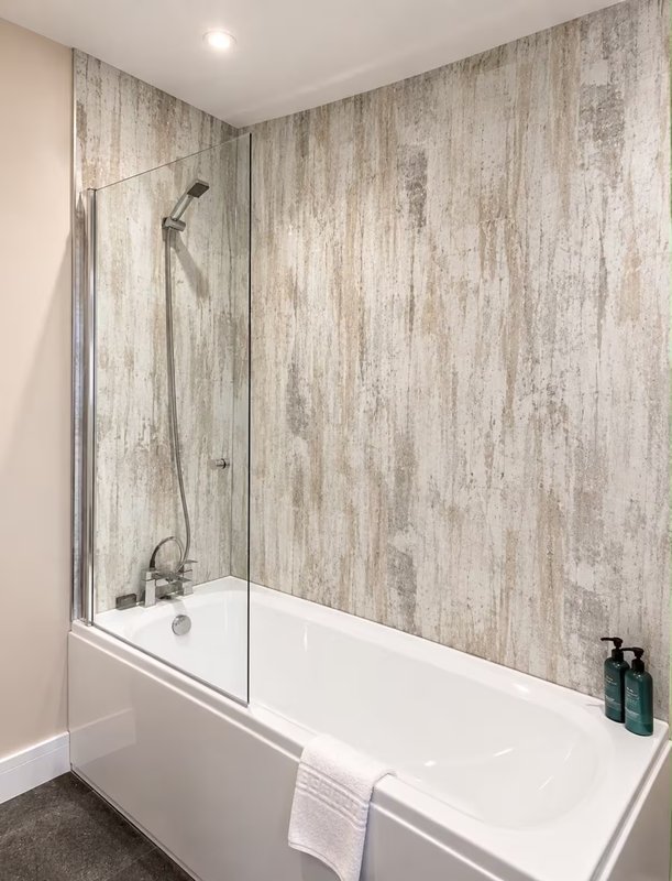 Modern bathroom with white bathtub, glass shower screen and wood-effect tile walls
