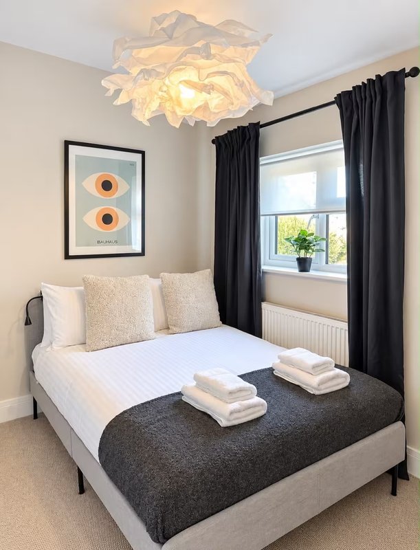 Bedroom with double bed, black curtains, ceiling light fixture and framed wall art