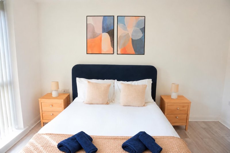 Modern bedroom with navy headboard, white bedding, wooden nightstands and abstract wall art