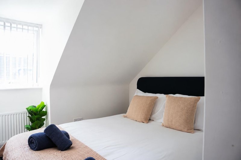 Attic bedroom with sloped ceiling, white bed, tan cushions and window with natural light