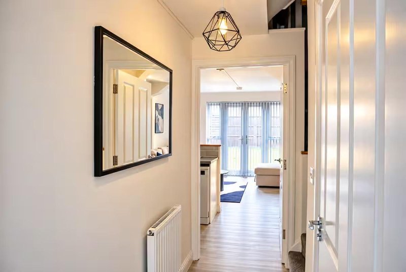 Bright hallway with framed mirror, geometric pendant light, radiator and open doorway to living area