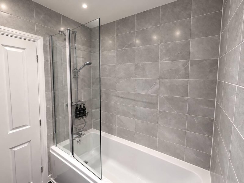 Modern bathroom with gray tile walls, walk-in shower enclosure, and white bathtub