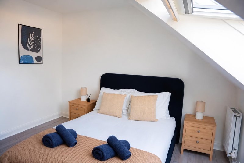 Bright attic bedroom with black bed frame, wooden nightstands, white bedding and decorative cushions