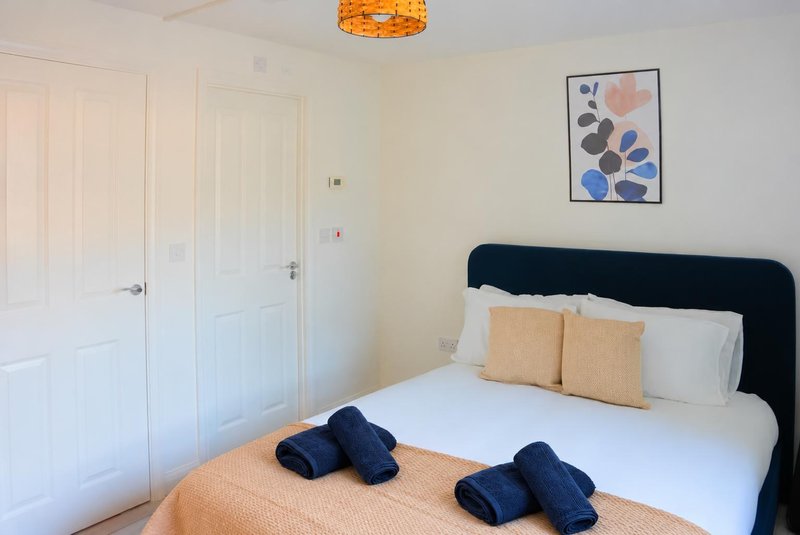 Bright bedroom with black headboard, white bedding, orange accent pillows and ceiling lamp