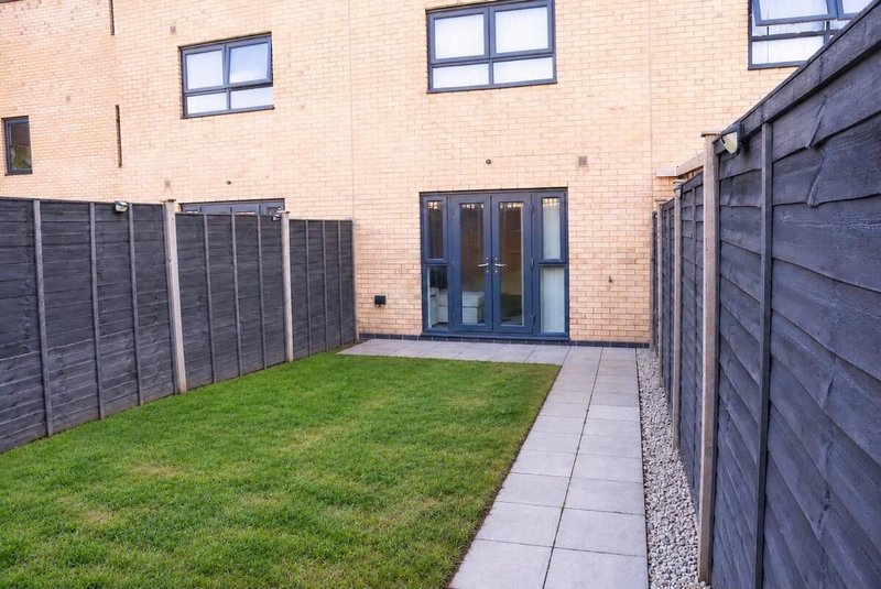 Modern brick property with patio doors, paved pathway, lawn and wooden fences