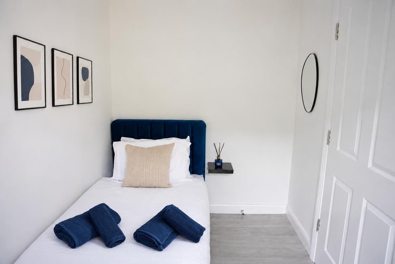 Modern bedroom with navy headboard, single bed, white bedding, and framed wall art
