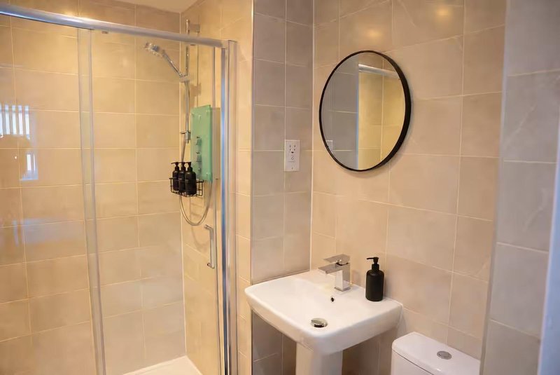 Clean bathroom with walk-in shower, pedestal sink, round mirror and beige tiles