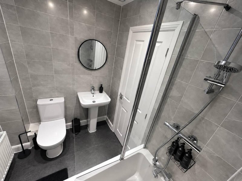 Modern bathroom with grey tiles, toilet, pedestal sink, circular mirror and walk-in shower