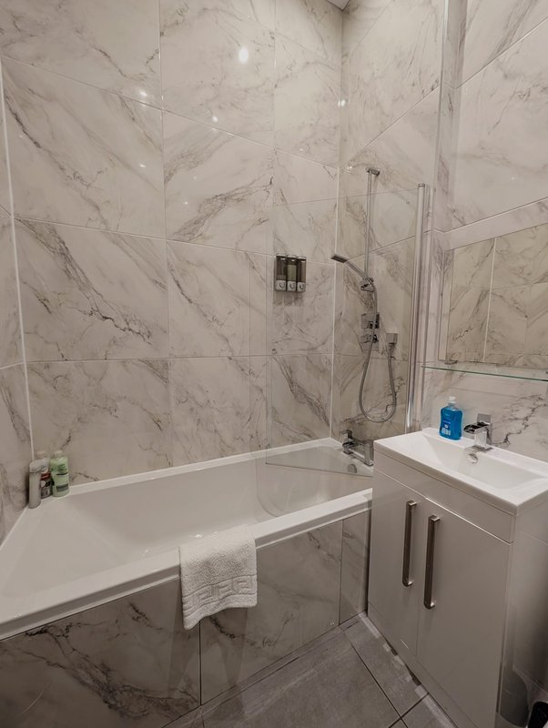 Modern bathroom with marble tiles, white bathtub, sink, and shower enclosure