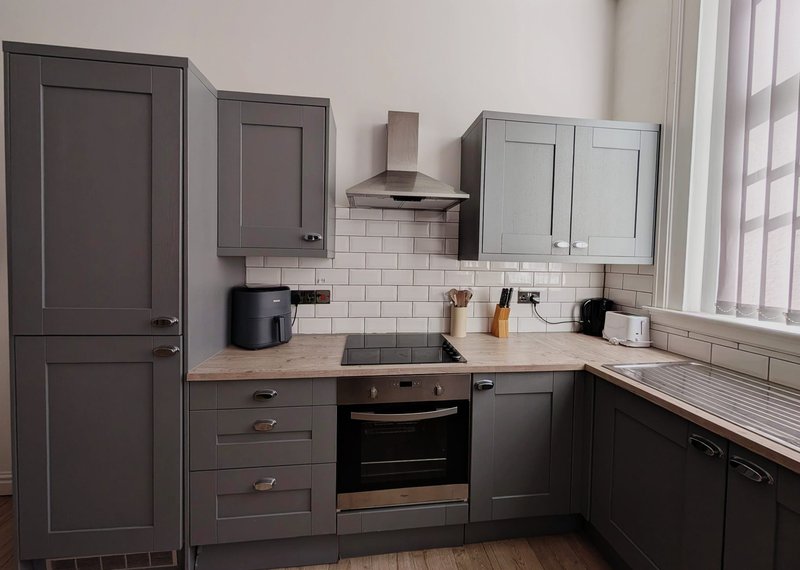 Modern kitchen with dark cabinetry, subway tile backsplash, stainless steel range hood and integrated appliances
