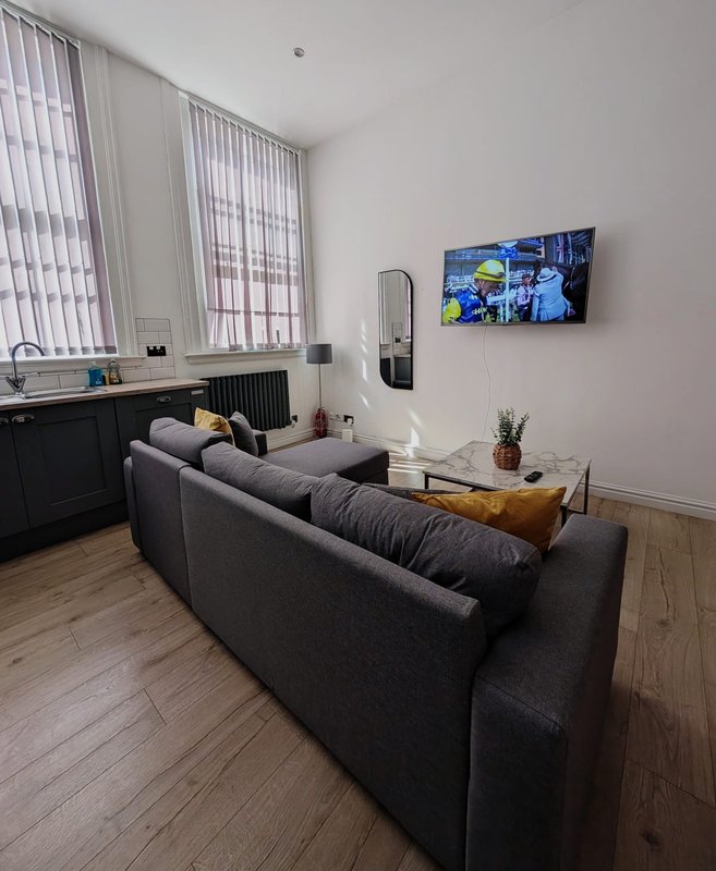 Modern living room with grey sofa, wooden coffee table, wall-mounted TV and vertical blinds