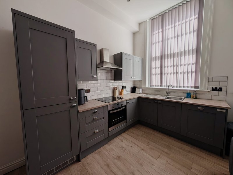 Modern kitchen with dark cabinetry, integrated appliances, white subway tile splashback, and wooden flooring