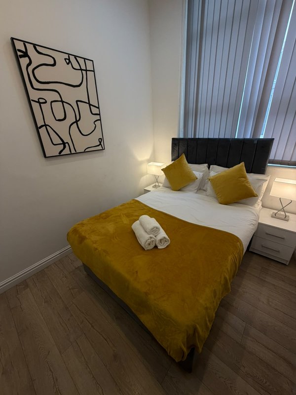 Modern bedroom with double bed, yellow bedding, cushions, white towels, and abstract wall art
