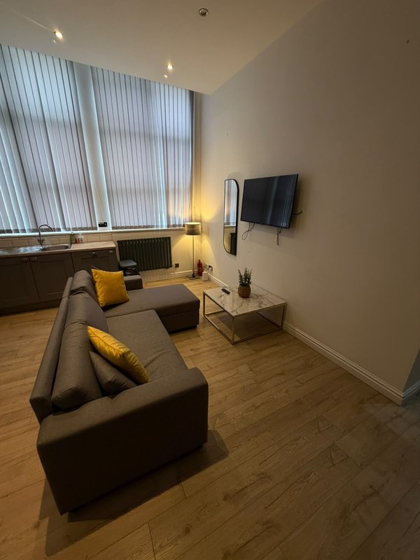 Modern living room with dark sofa, yellow cushions, wall-mounted TV and wooden flooring