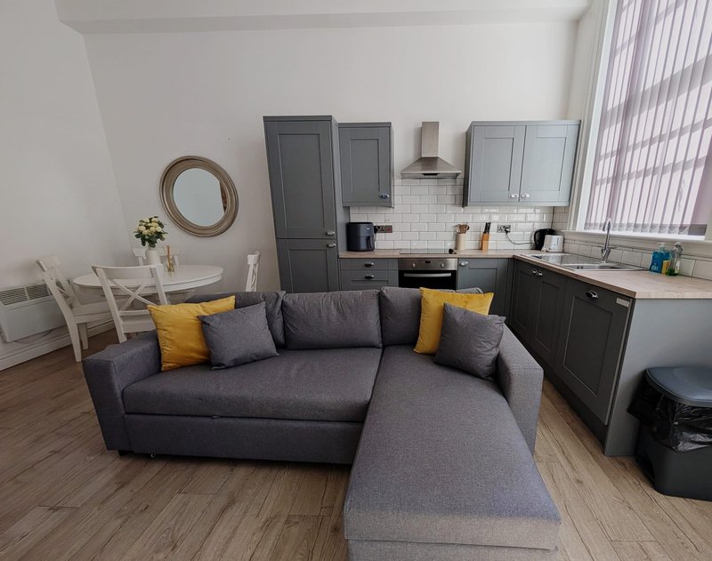 Open-plan living and kitchen with grey sofa, yellow cushions, dining area and fitted kitchen