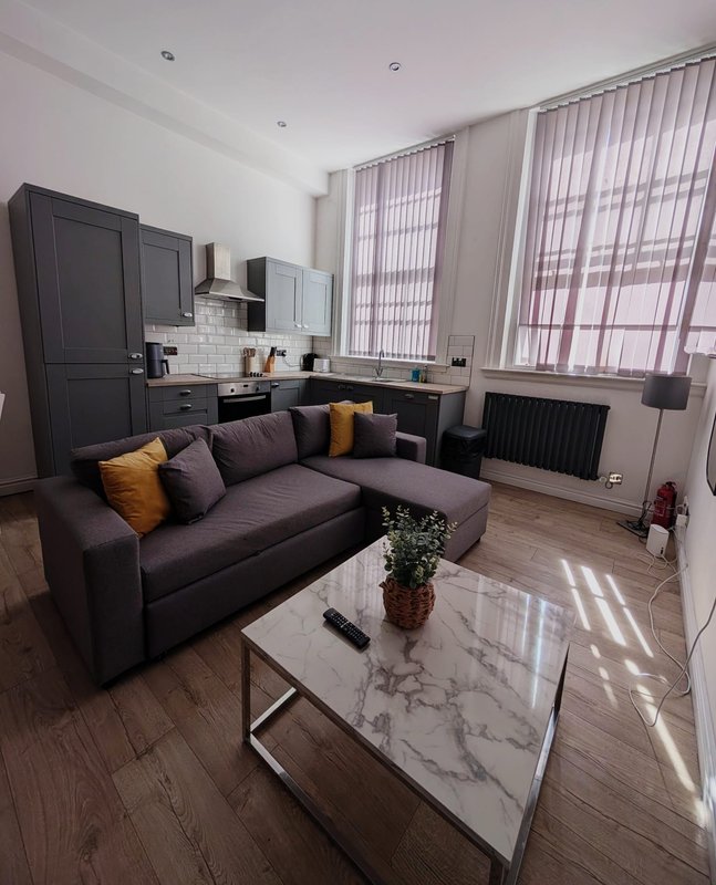 Modern open-plan living room with purple sofa, marble coffee table, kitchen area, and large windows with blinds