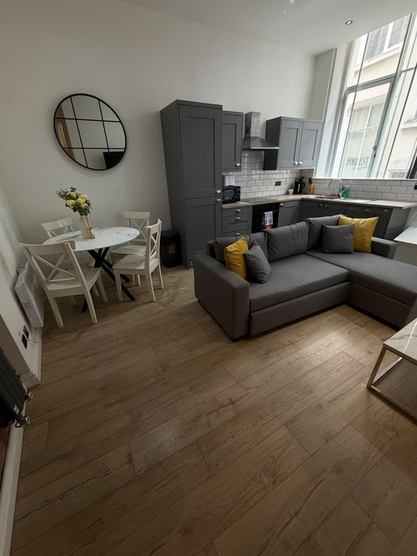 Modern open-plan studio with grey sofa, dining table, kitchenette and round mirror