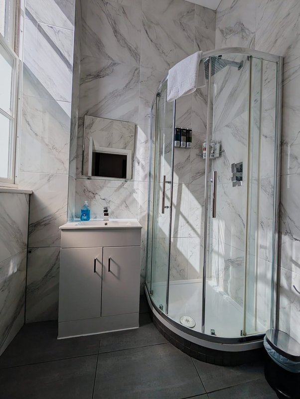 Modern bathroom with marble-effect tiles, white vanity unit, and curved glass shower enclosure