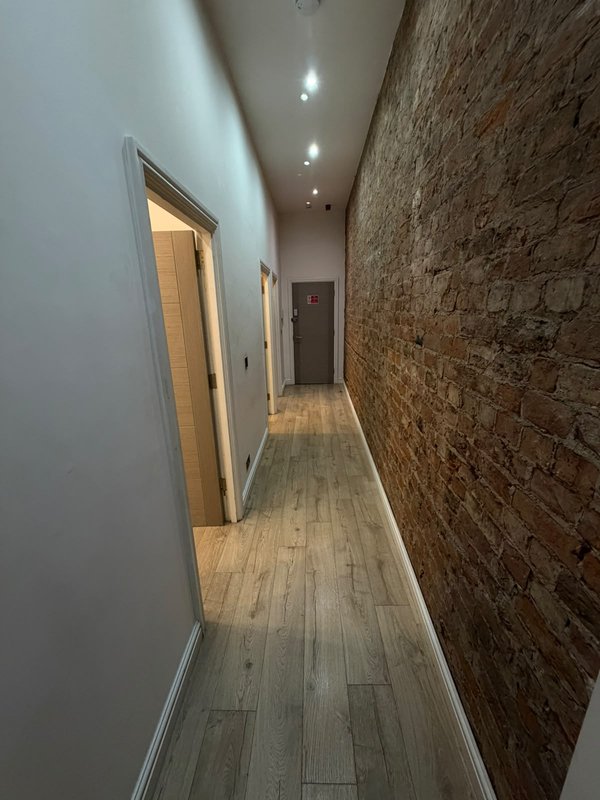 Long narrow hallway with white walls, exposed brick, wooden flooring and recessed lighting
