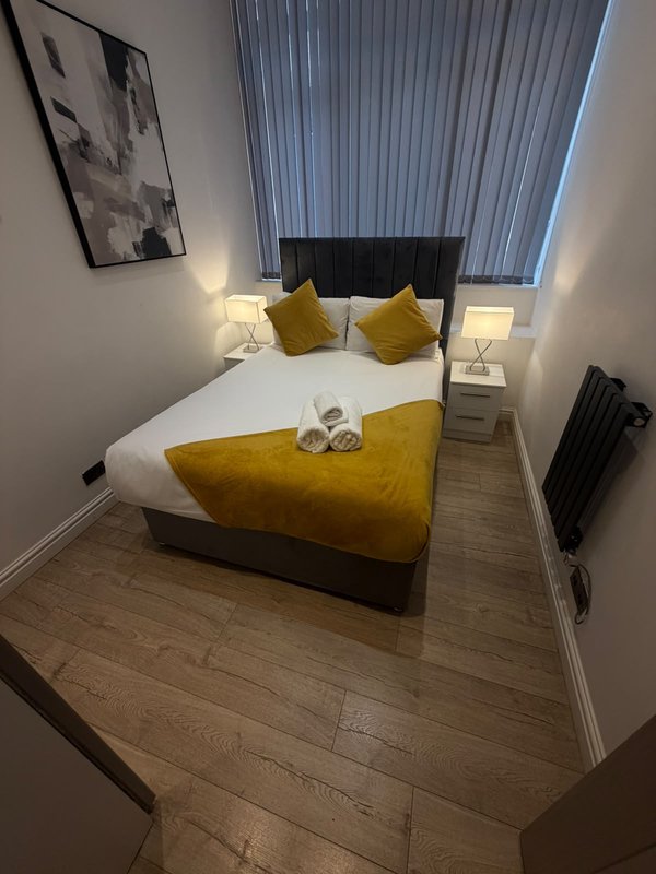 Modern bedroom with double bed, yellow cushions, bedside lamps, and vertical blinds