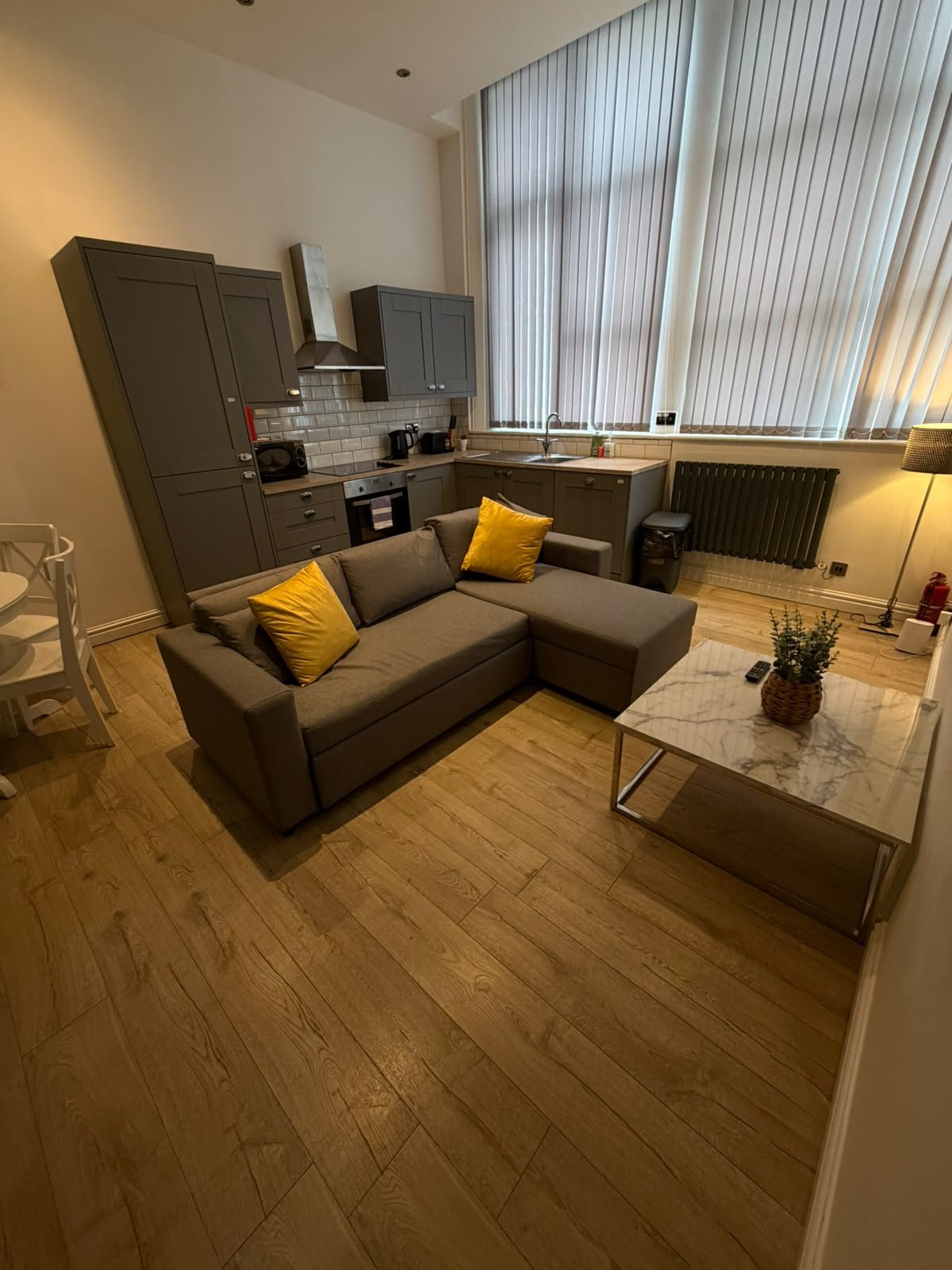 Modern studio apartment with grey sofa, yellow cushions, kitchenette and desk seating area