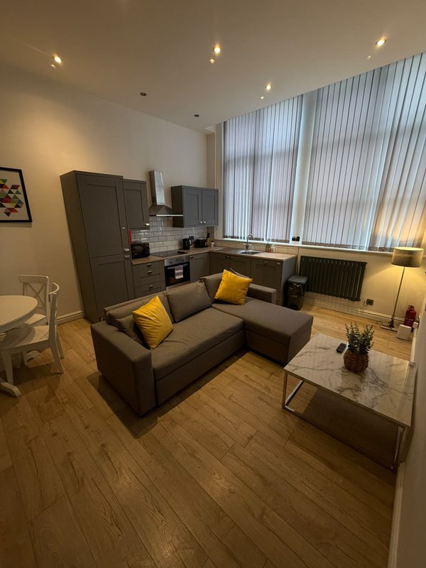 Open-plan studio with grey sofa, kitchenette, wooden flooring and vertical blinds