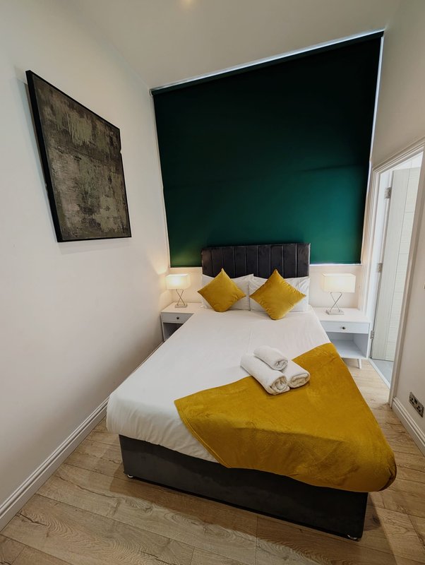 Modern bedroom with double bed, yellow cushions, green feature wall, and framed artwork