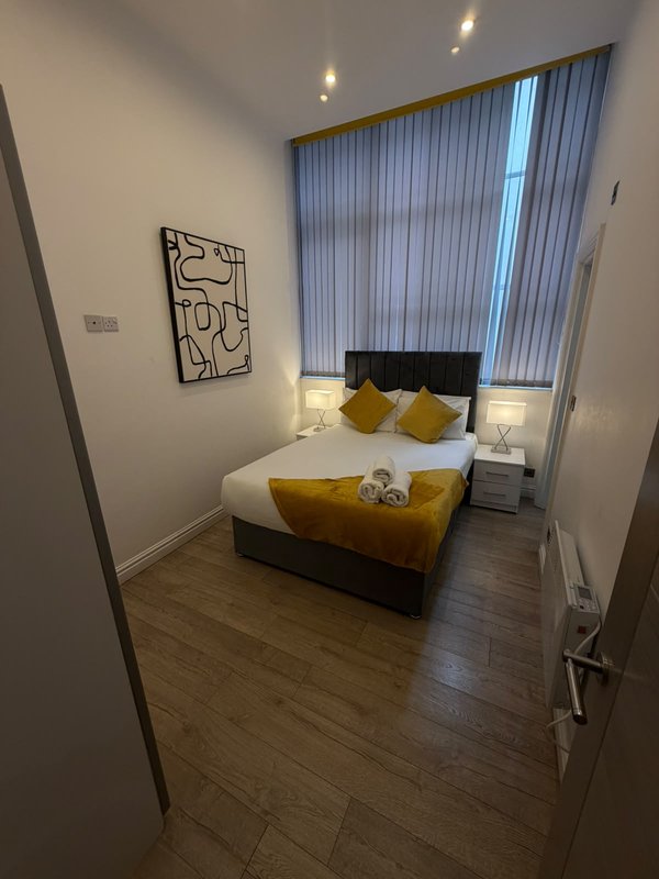 Modern bedroom with double bed, yellow cushions, dark wood flooring and vertical blinds