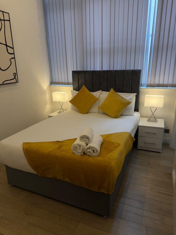 Modern bedroom with double bed, black headboard, yellow cushions and throw, bedside lamps and tables