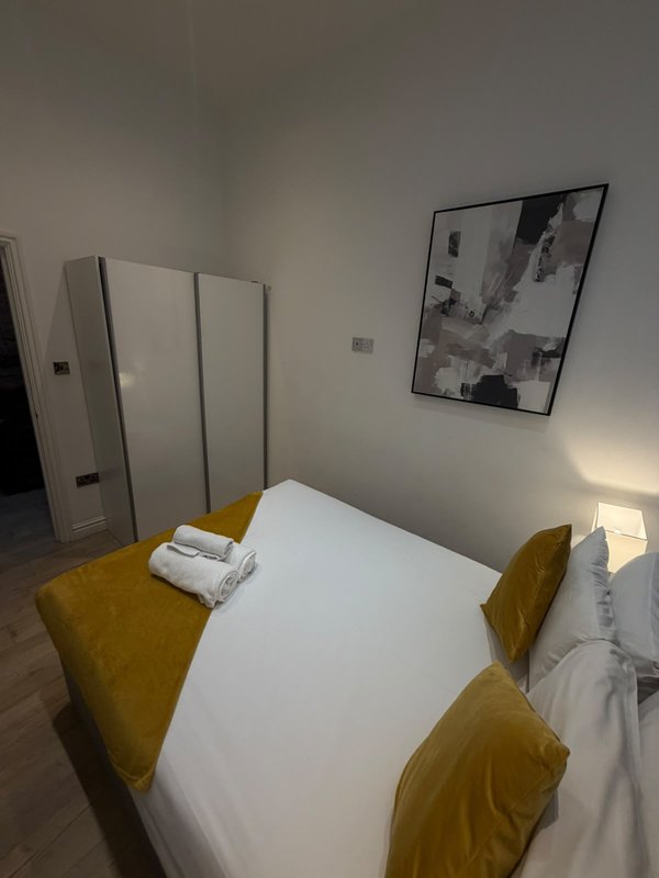 Modern bedroom with white bed, mustard-yellow chairs, framed wall art, and folding screen