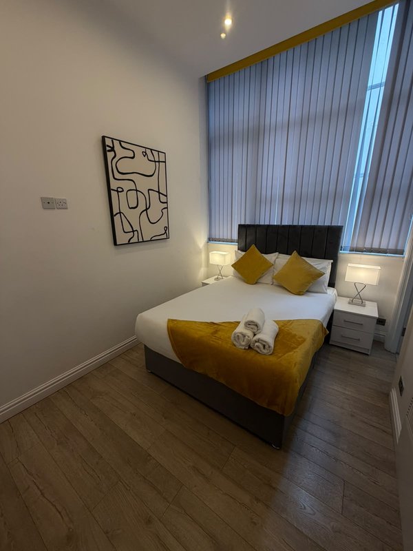 Modern bedroom with double bed, yellow cushions, wall art, and vertical blinds