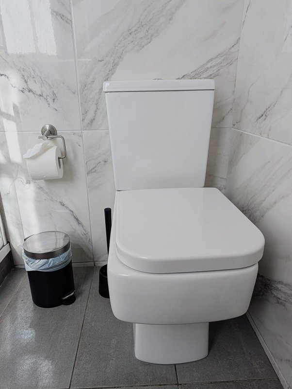 Modern bathroom with white toilet, marble-effect wall tiles, and toilet brush holder