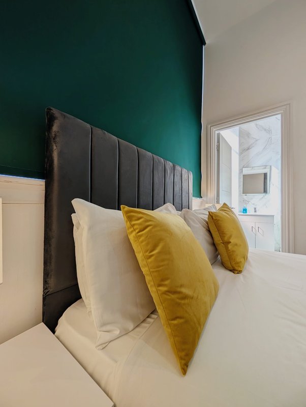 Modern bedroom with black padded headboard, white duvet, and yellow decorative pillows