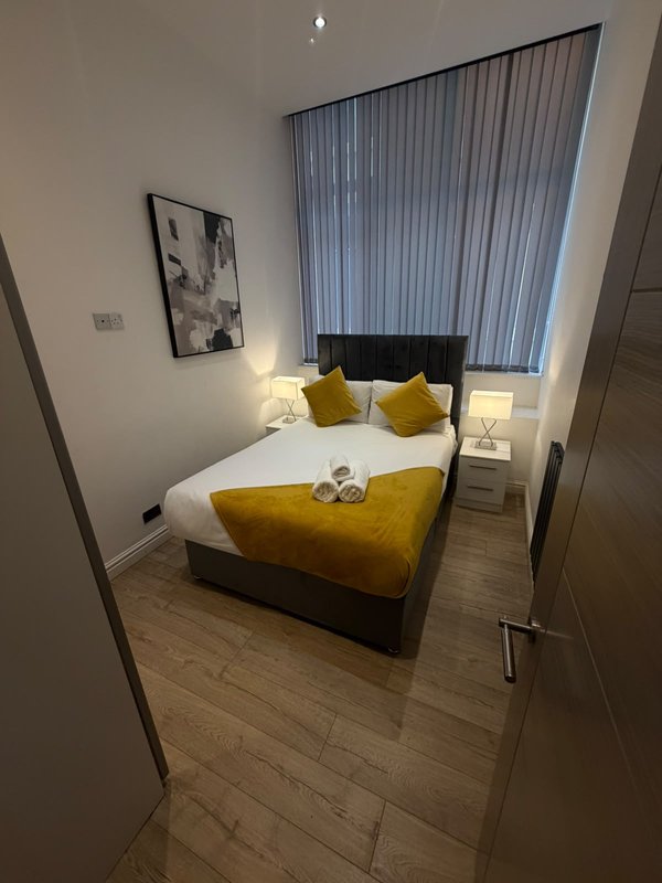 Modern bedroom with double bed, yellow cushions, vertical blinds and bedside lamps