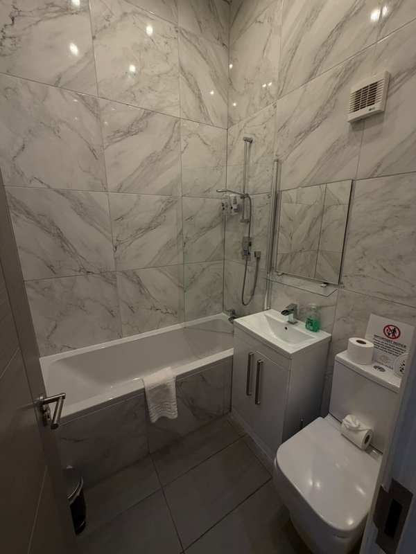 Modern bathroom with marble-effect tiling, bathtub, vanity sink, toilet and recessed lighting