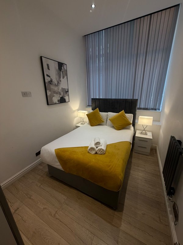 Modern bedroom with double bed, mustard yellow throw, white bedding, framed wall art, and vertical blinds