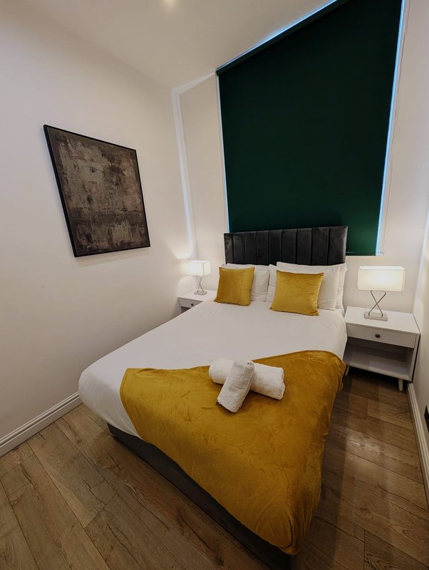 Modern bedroom with double bed, mustard-yellow cushions, dark headboard and green accent wall