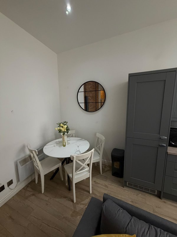 Modern dining area with round white table, two white chairs, wall mirror and dark door
