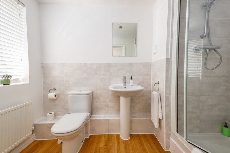 Modern bathroom with toilet, pedestal sink, shower enclosure and wooden floor