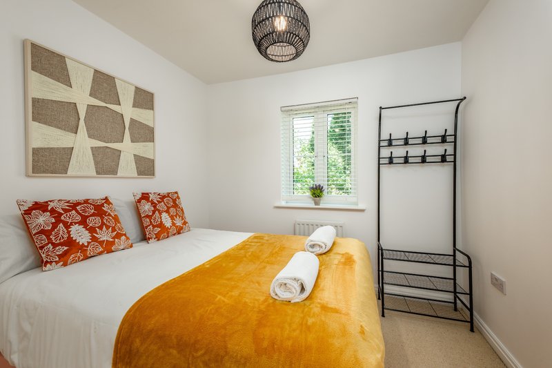 Bright bedroom with double bed, orange throw, patterned pillows and geometric wall art