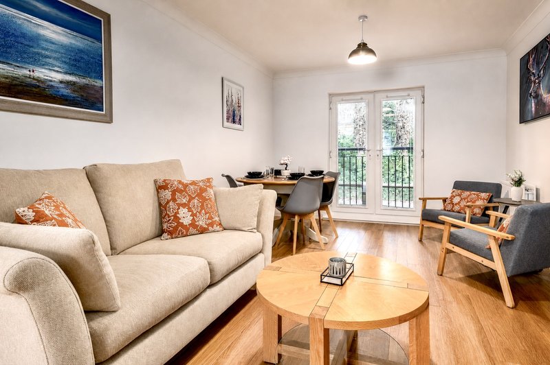 Open-plan living room with beige sofa, wooden table, dining area and glass doors to balcony