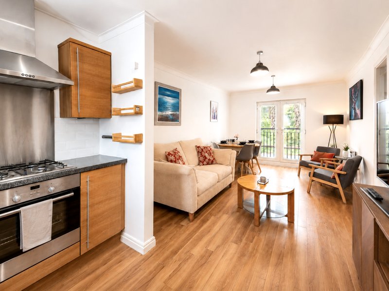Open-plan kitchen and living room with wooden cabinetry, cream sofa, and hardwood flooring
