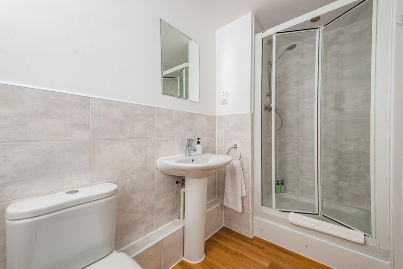 Modern bathroom with toilet, pedestal sink, shower enclosure and wooden flooring