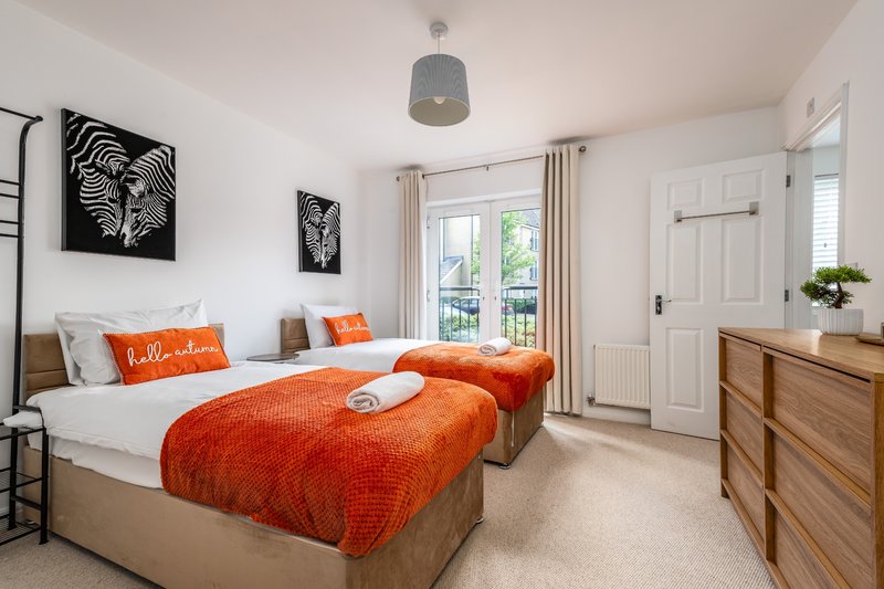 Bright twin bedroom with orange bedding, wooden furniture, wall art and glass doors to balcony