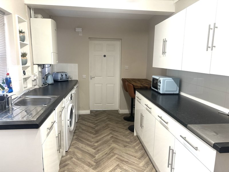 Galley kitchen with white cabinets, black countertops, herringbone flooring and appliances