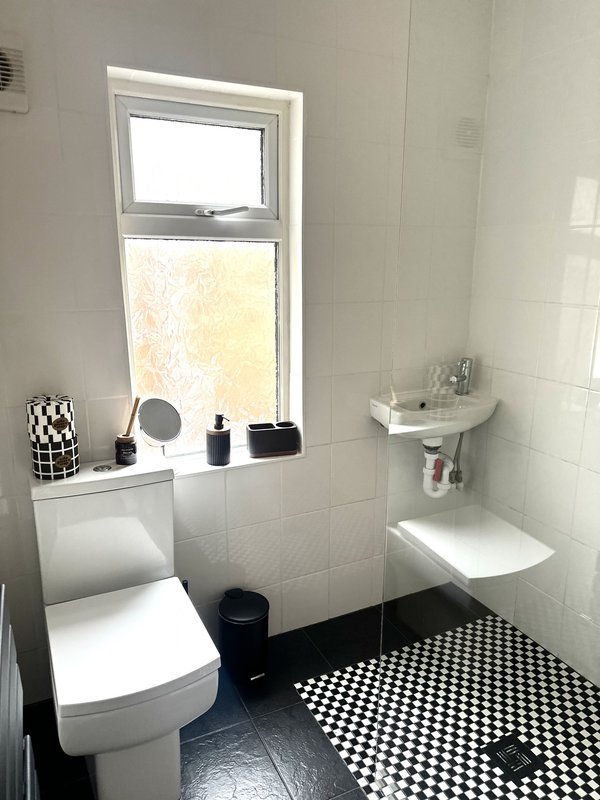 Small bathroom with toilet, sink, window, checkered floor and toiletries on windowsill
