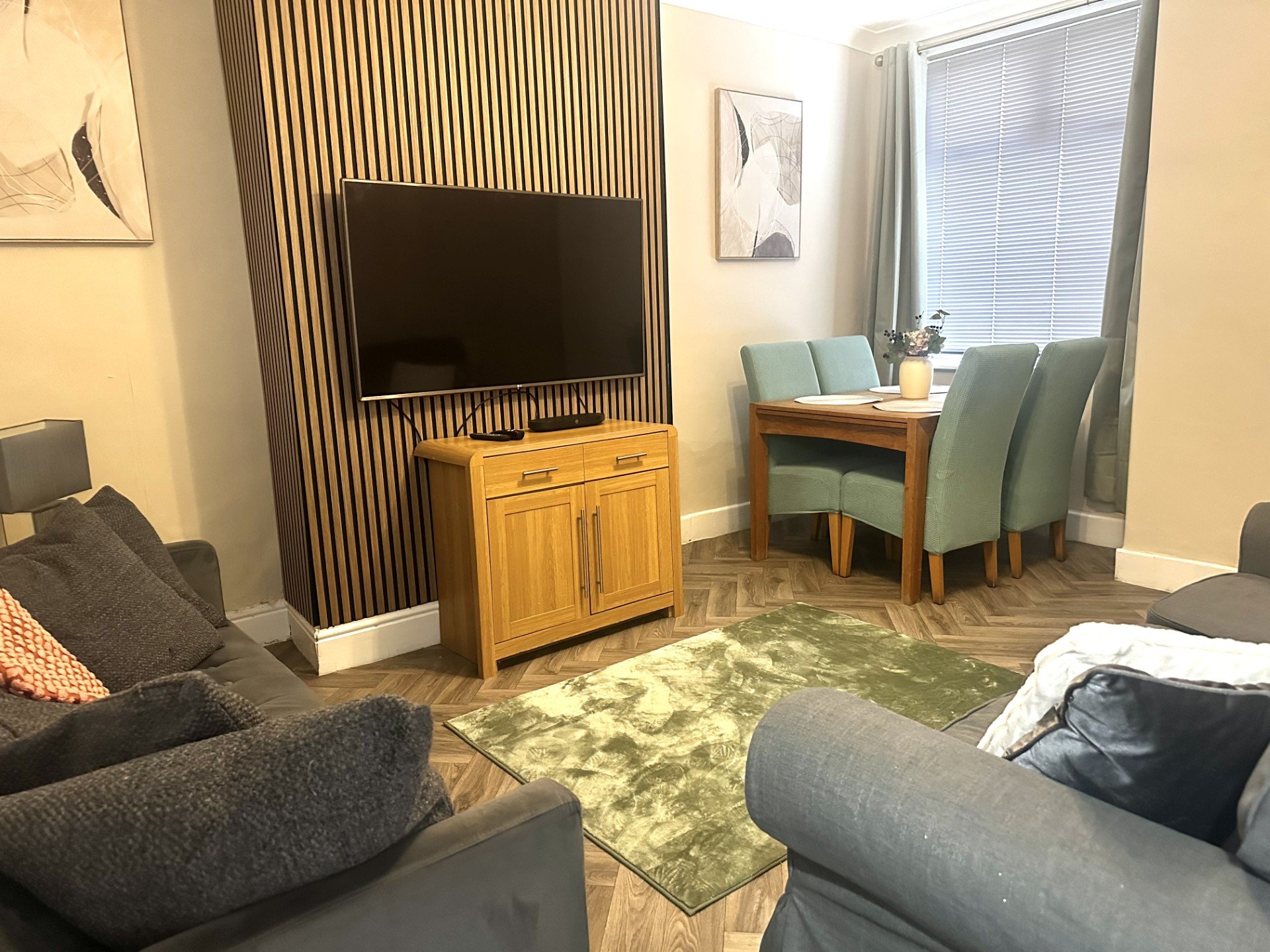 Living room with grey sofas, wooden TV stand, blue chairs, window with blinds and wall art