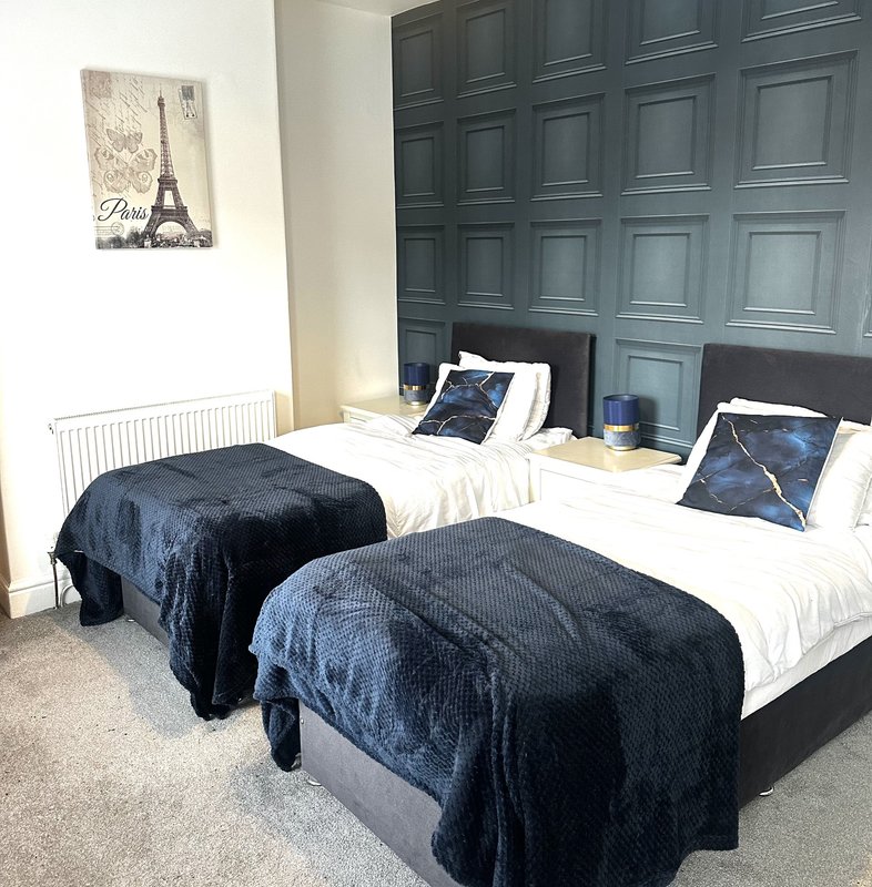 Twin bedroom with dark headboard, navy bedding, white pillows, and Paris wall art
